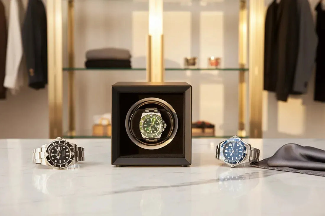 Three luxury stainless steel dive watches displayed on a marble surface with a black automatic watch winder.
