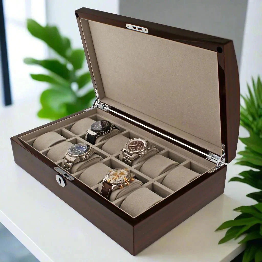 The Aevitas 12 Watch Box in striped mahogany wood veneer sits open on a white surface, revealing its beige interior and luxury timepieces, with green plants in the background for an elegant display.