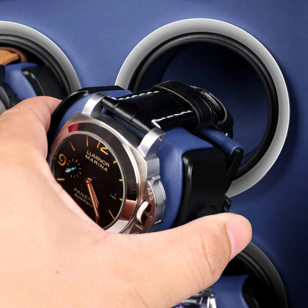 Hand placing a luxury watch onto a black and blue leather Aevitas watch winder with silver accents.