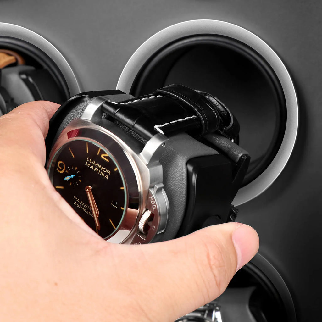 Hand placing a luxury watch into a black vegan leather Aevitas watch winder with a sleek grey interior and silver trim.
