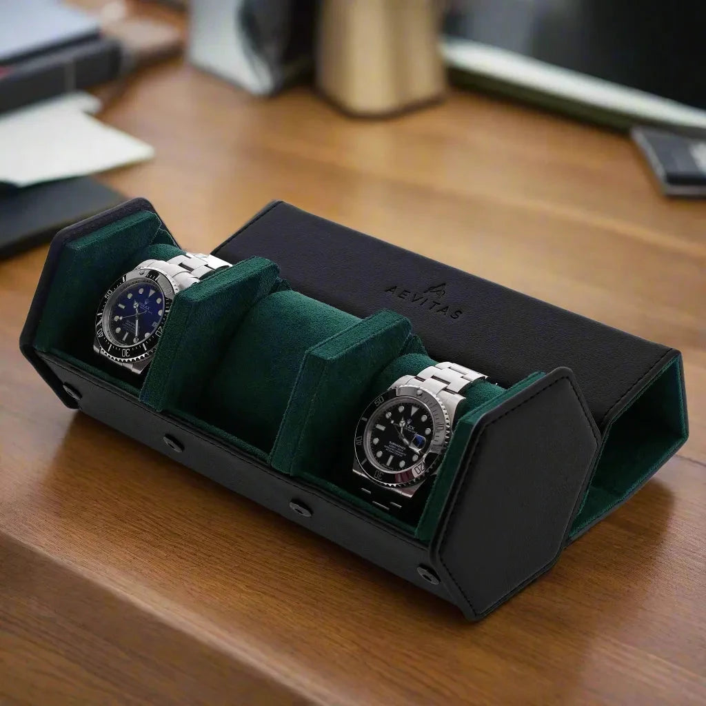 The Aevitas Watch Winders 3 Watch Travel Case in black leather with green lining, hexagon style, holds two silver wristwatches and sits on a wooden desk with papers and a laptop in the background.