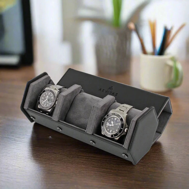 The Aevitas Watch Winders 3 Watch Travel Case in black leather with grey lining and hexagon style holds two silver watches on a wooden desk, with a blurred background of a mug with pencils and a plant.