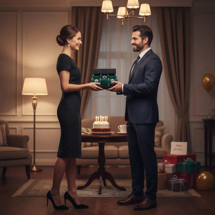 A woman in a black dress and a man in a suit exchange an Aevitas Watch Winders 6 Watch Travel Case in Black Leather with Green Lining (Hexagon Style) gift box, surrounded by birthday cake, candles, and wrapped presents in an elegant, warmly lit room.