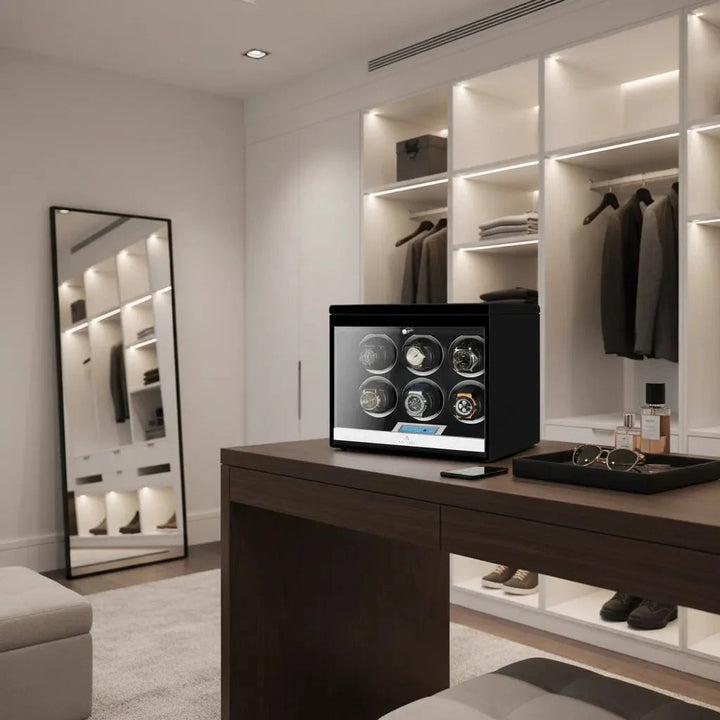 A modern walk-in closet with an open wardrobe, clothes on hangers, large mirror, and wooden table. On the table is the Aevitas 6 Watch Winder Black Edition with Extra Storage Area, next to sunglasses and bottles.