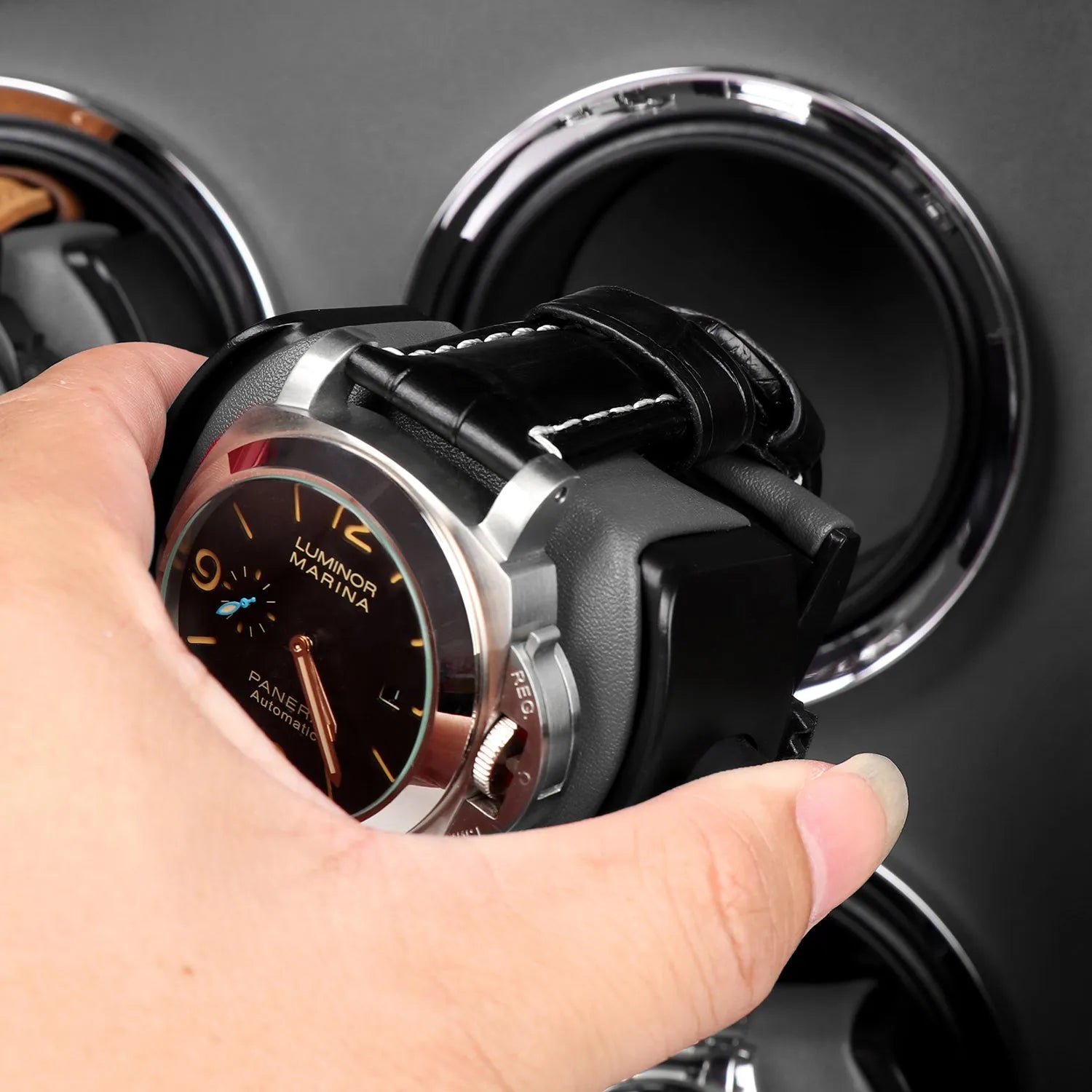 Hand placing a luxury watch onto a black leather Aevitas winder holder with a sleek grey lining and silver trim.