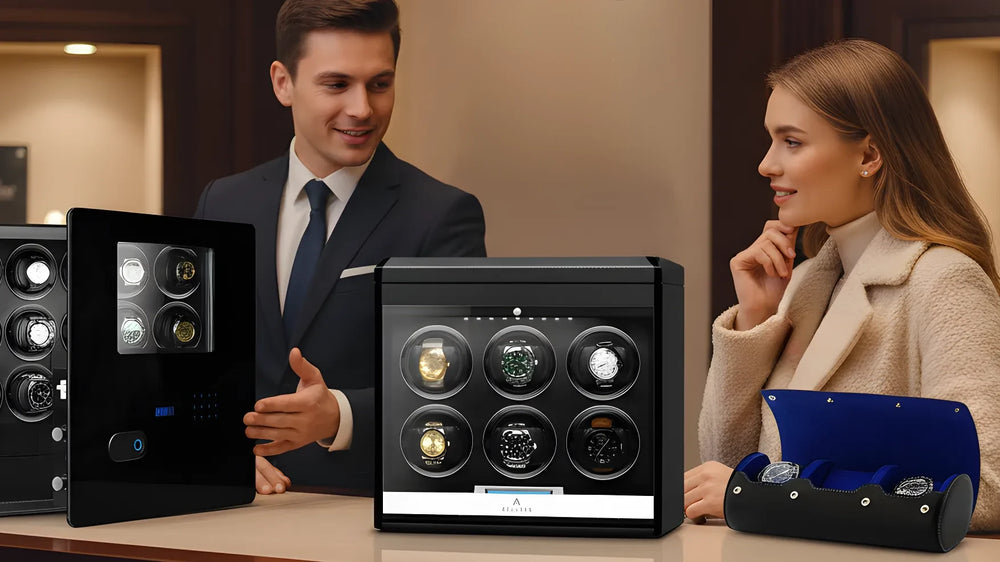 A man in a suit and a woman in a coat talk at a counter displaying luxury watch winders and a blue watch case, with holiday decorations in the background.