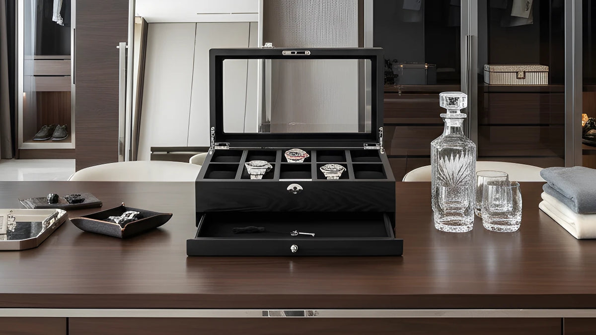 Black watch box with open lid displaying watches on a wooden table.
