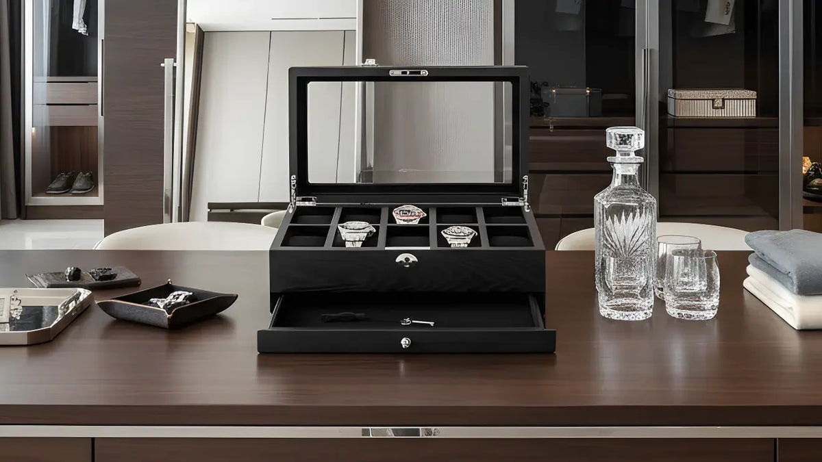 Black watch box with open lid displaying watches on a wooden table.