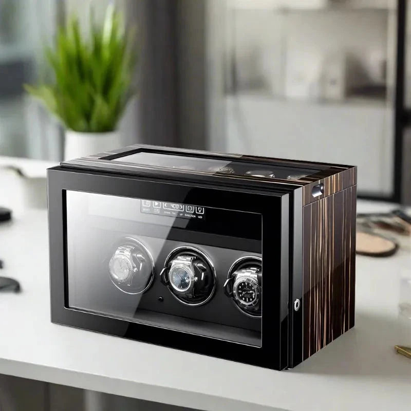 The Aevitas Premium 3 Watch Winder with Storage in Zebrano Ebony Wood is displayed on a white desk in a modern, bright room featuring a green plant and softly blurred background decor.