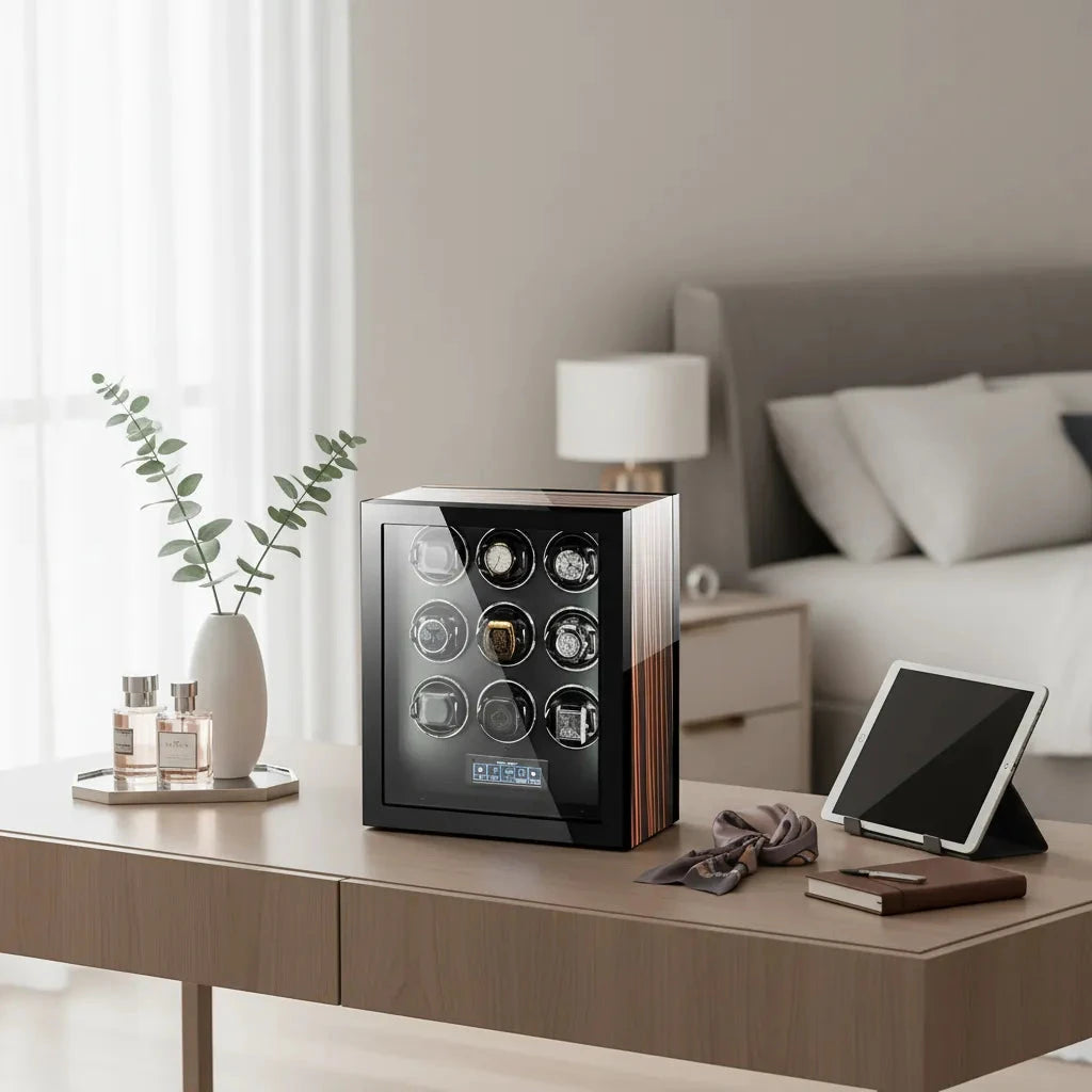 A modern beige bedroom features a desk displaying the Aevitas Premium Automatic 9 Watch Winder with Touch Screen, a tablet, striped tie, tray of perfume bottles, and a vase with green leafy branches.
