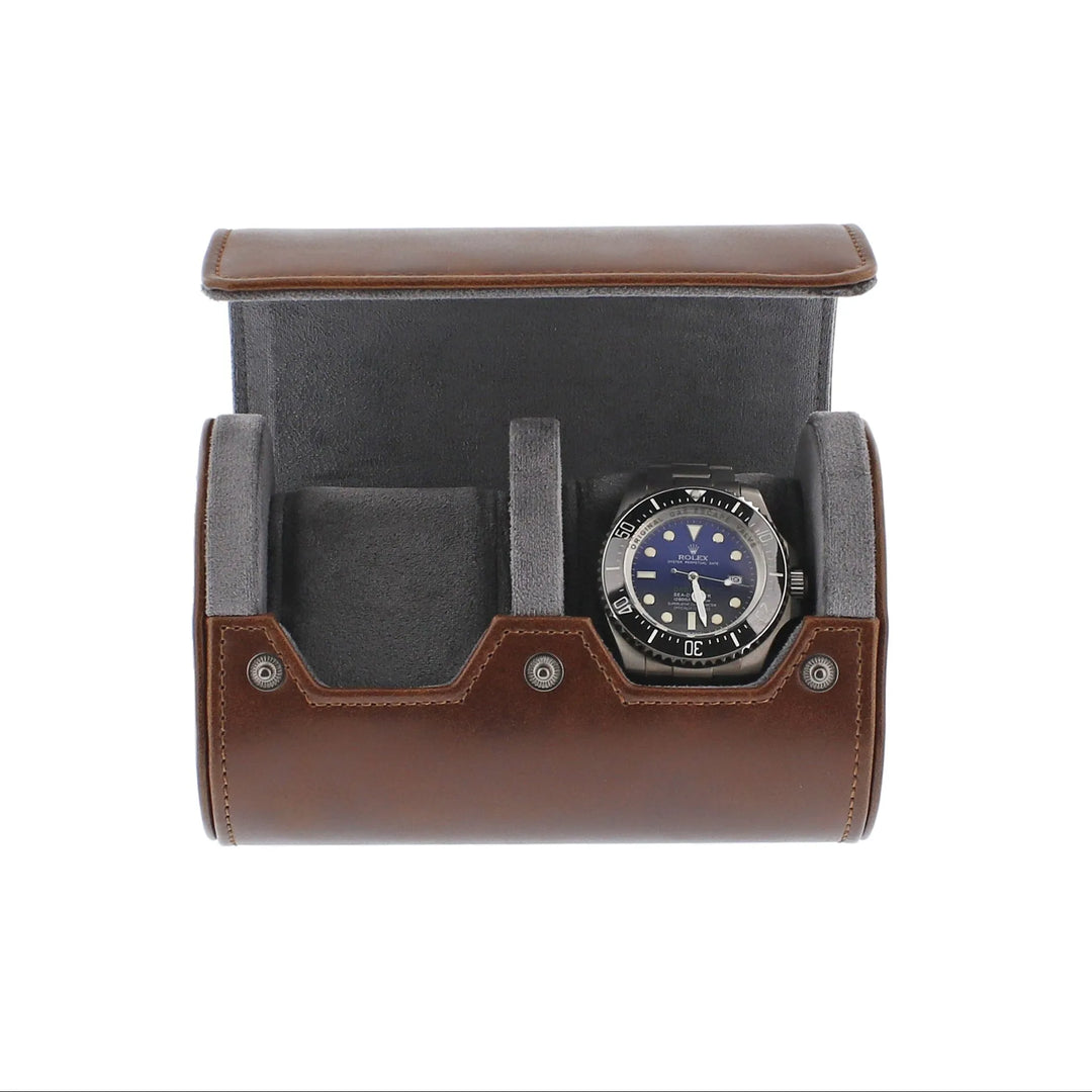 The Aevitas Premium Double Watch Roll in vintage brown leather with super soft grey suede lining is open to show two compartments, one holding a black and silver watch with a blue face, set against a white background.