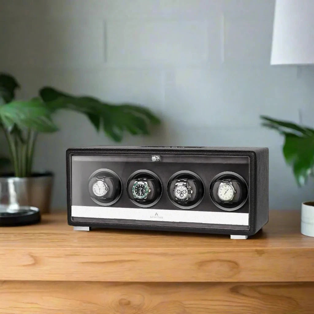 The Aevitas Premium Quad Watch Winder in black genuine leather, mains powered, elegantly displays four automatic watches on a wooden surface with a potted plant and white lamp in the background.