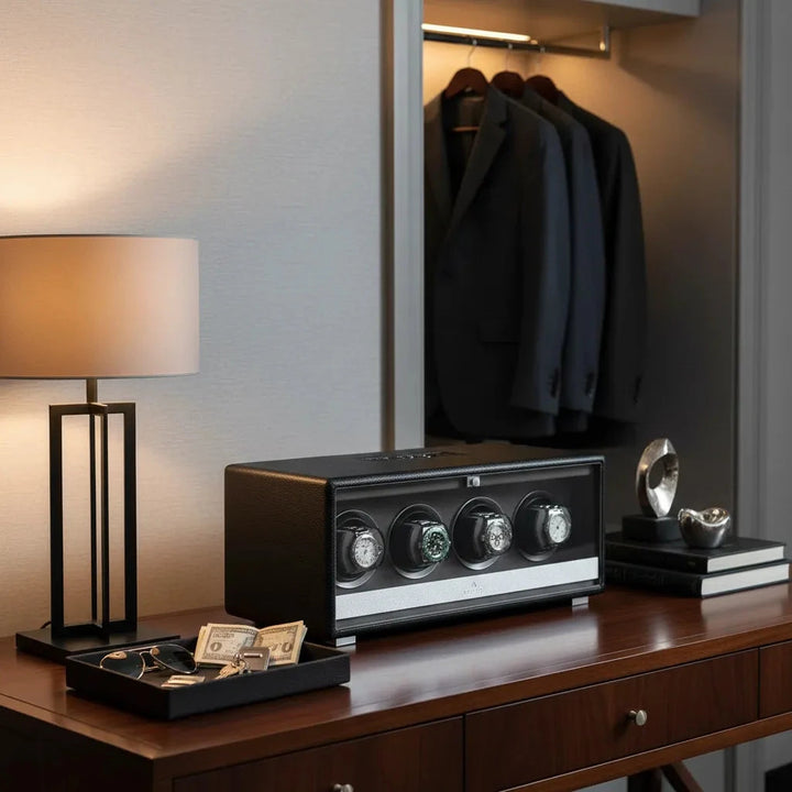 A modern wooden dresser holds an Aevitas Premium Quad Watch Winder in black leather, lamp, cash, keys, glasses, and books. Suits hang neatly in the open closet behind, making for an organized and elegant setting.