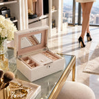 Open ivory jewellery box with velvet lining displayed on a glass vanity in a modern dressing room.