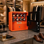 Elegant watch winder safe in orange leather shown on textured surface in a sophisticated dressing room, surrounded by stylish accessories and soft lighting.
